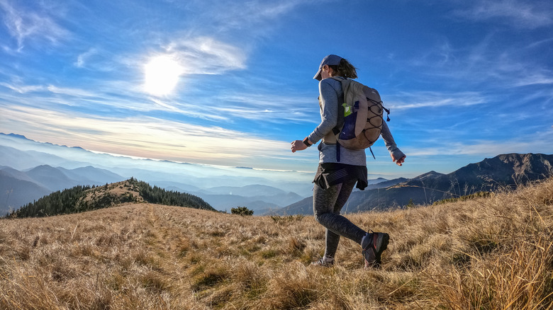 a woman walks with a backpack with mountains on the horizon